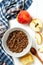 Chocolate granola in a white bowl in a composition with honeycombs, a spoon, apple on white wooden background. Healthy breakfast