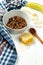 Chocolate granola in a white bowl in a composition with honeycombs, a spoon, banana on white wooden background. Healthy breakfast