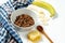 Chocolate granola in a white bowl in a composition with honeycombs, a spoon, banana on white wooden background. Healthy breakfast