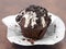 chocolate muffin with white glaze and dark cookie crumbs on brown background, unpacked cupcake