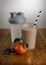 Chocolate orange milkshake, ingredients and shaker with paper straw on a wooden table top