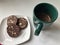 Chocolate sausage, cut in rings, lies on a saucer. Nearby is coffee in a green mug.