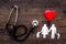 Choose family health insurance. Stethoscope, paper heart and silhouette of family on dark wooden background top view