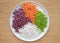 Chopped asparagus, carrot, radish and sweet purple potatoes on white plate against wooden background