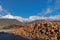 Chopped down tree trunks, cut pine logs stacked in a storage yard and beautiful mountain landscape in the background, in winter