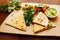 Chopped triangles of quesadillas with vegetables and herbs and sauce on wooden board