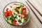 Chopped vegetables - cucumbers, tomatoes and onions in glass bowl and chopstick on bamboo mat. View from above. Copy space