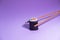 Chopsticks taking a salmon and avocado maki on purple background. Japanese cuisine. Conceptual picture. Copy space