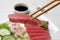 Chopsticks with tasty sashimi (piece of fresh raw tuna) against blurred background, closeup