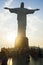 Christ the Redeemer on top of Corcovado with sunset in the background and many tourists around the monument.