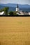 Christian church as an part of village, forested hills in background, yellow field of grain in foreground