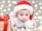 Christmas baby. Cute  curious  four month old  caucasian baby in a Santa Claus hat looking at camera near big present