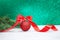 Christmas ball with red bow and twisted ribbon with spruce branches. Behind blurred green background. New Year