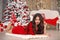 Christmas. Beautiful santa girl. Smiling woman with long hair and red lips makeup lying on white knitted chunky yarn blanket in