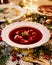 Christmas beetroot soup, borscht with small dumplings with mushroom filling in a ceramic white plate on a holiday table.