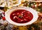 Christmas beetroot soup, borscht with small dumplings with mushroom filling in a ceramic white plate on a holiday table.