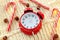 Christmas candy cane, garland and red alarm clock on white knitted background. Winter minimalistic flat lay. Waiting for holiday.