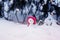 Christmas card with a festive cute toy snowman in a bright pink cap sitting in a snowdrift with a gift under the Christmas tree in