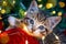 Christmas cat. Portrait striped kitten playing with Christmas lights garland on festive red background. Kitty looking at