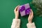 Christmas celebration concept. First person top view photo of woman`s hands in white knitted jumper holding lilac giftbox with