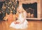 Christmas, celebration, holiday, xmas concept - happy little girl with gifts near christmas tree and fireplace