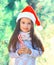 Christmas child little girl in santa red hat with sweet lollipop cane near branch tree