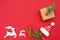 Christmas composition: pine branches, gift box, cinnamon sticks, wooden deers and santa hat on red background. Space for text. Top