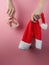 Christmas concept. Female hands hold santa hat and gift box on pink pastel background