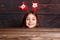 Christmas concept. Little funny girl in deer horns doing surprise on wooden background