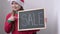 Christmas cute little Santa girl smiling shows billboard with sign sale. Adorable child in red Santa hat holding