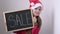 Christmas cute little Santa girl smiling shows billboard with sign sale. Adorable child in red Santa hat holding