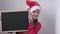 Christmas cute little Santa girl smiling shows blank empty billboard sign. Adorable child in red Santa hat holding black