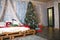 Christmas decor in the bedroom in the loft style. The bed is made of wooden pallets with white linen and red blankets and pillows.