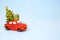 Christmas decor - a red retro car carries a Christmas tree with gift boxes on the roof. Toy with sequins on a blue background,