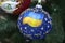 Christmas decoration, with Ukrainian national flag painted, hanging on a Christmas tree before New Year Day