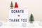 Christmas donation, charity. Donate and Thank you message on lightbox. Christmas decoration and garland on white desk
