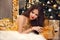 Christmas elegant girl lying in golden dress with expensive jewelry set on party over gift boxes. Healthy long hair style. Makeup