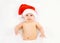 Christmas and family concept - cute funny baby in red santa hat lying on white bed home, humor, joke