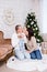 Christmas and family concept - happy young parents kissing cute little baby girl daughter near decorated christmas tree