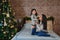 Christmas family portrait of happy smiling mother sitting on bed and hugging small daughter near to christmas tree at home