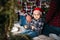 Christmas family portrait of young happy smiling parents playing with small kid in red santa hat near the christmas tree. Winter