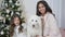Christmas family, sisters are posing on camera sitting at sofa with a white dog
