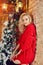 Christmas Fashion woman blonde in the red sweater, having fun and posing against the Christmas tree and lamppost. Winter