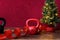 Christmas fitness, red kettle bell, with artificial Christmas tree and white lights, red ribbon, wood table, red background