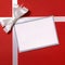 Christmas gift card or label and envelope, white ribbon bow, red wrapping paper background, copy space