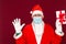 Christmas gift. Santa Claus palms at tops wears medical mask holding gift box and looking at camera