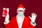 Christmas gift. Santa Claus palms at tops wears medical mask holding gift box and looking at camera