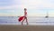 Christmas Girl Santa Claus walking at ocean sandy beach with large red bag full of presents - New Year vacation and