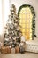 Christmas green artificial fir tree in a bright room of the house near a large floor-to-ceiling window with yellow light. Decorate