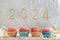 Christmas greeting card with cupcakes and gold sparklers numbers 2024. Holiday muffins with pink buttercream frosting